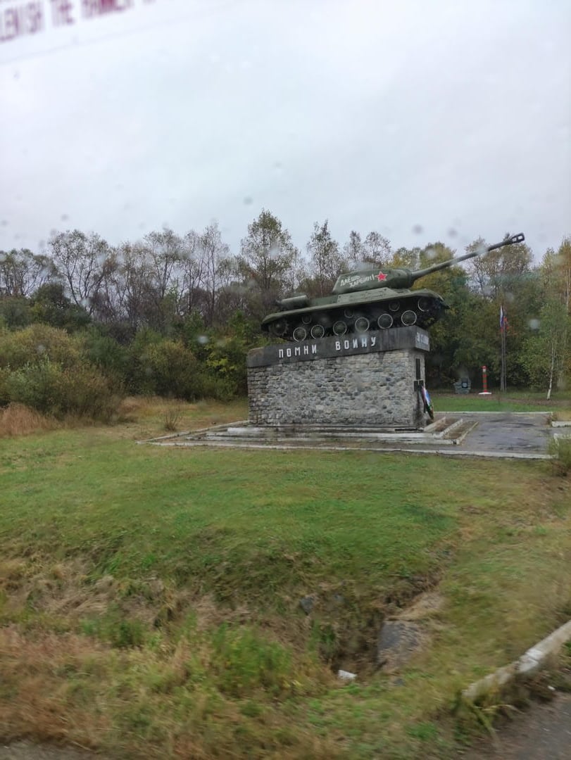 一座坦克纪念碑,坦克上有一个红星标志,周围是草地和树木。
