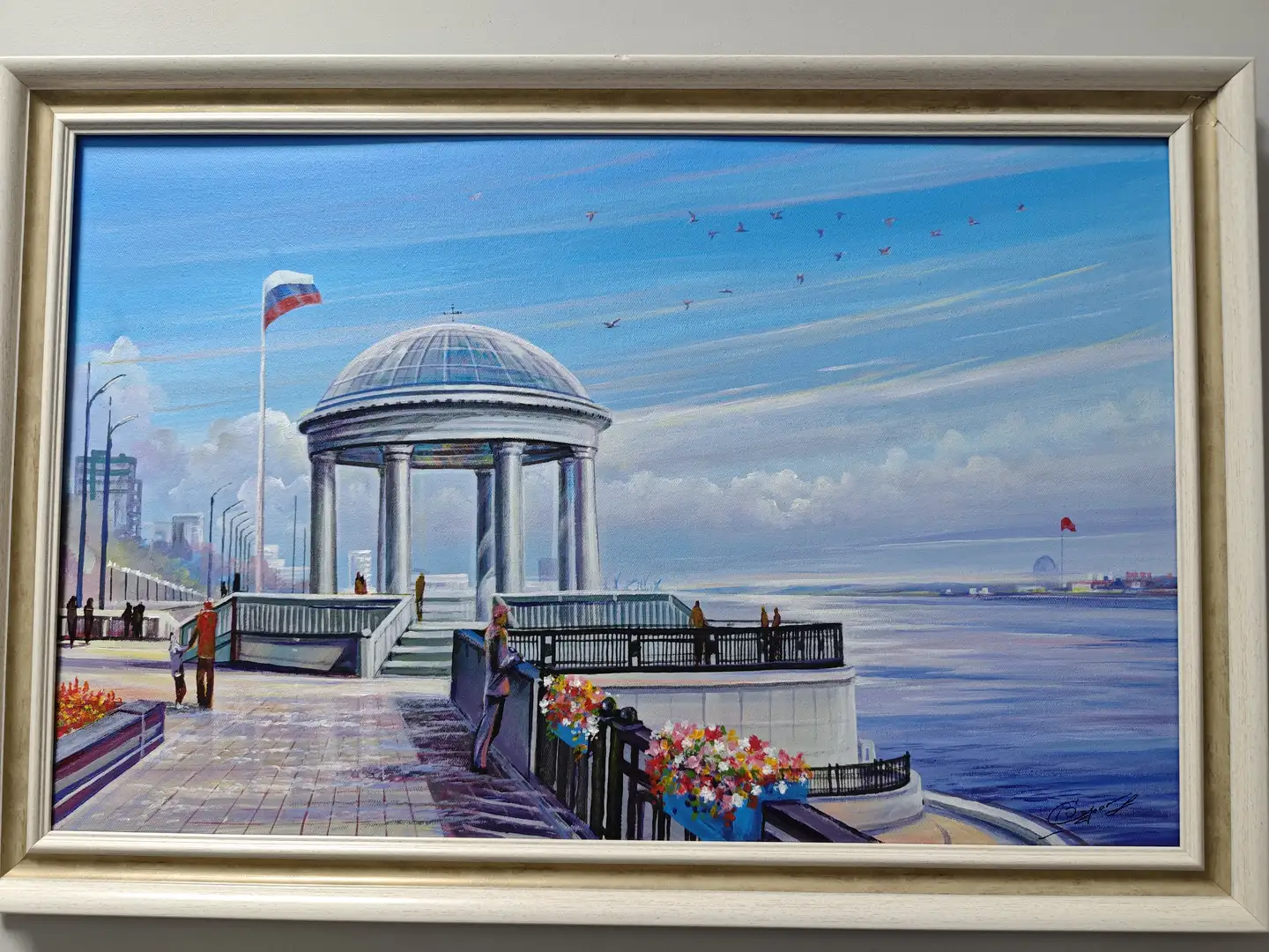 一幅白色画框中的油画,描绘了一个临水的圆形亭子,亭子由多根柱子支撑,顶部为玻璃穹顶。画面左侧有行人和旗帜,右侧是宽阔的水面,远处可见城市轮廓和飞翔的鸟群。前景中有花坛和栏杆,整体色调明亮。