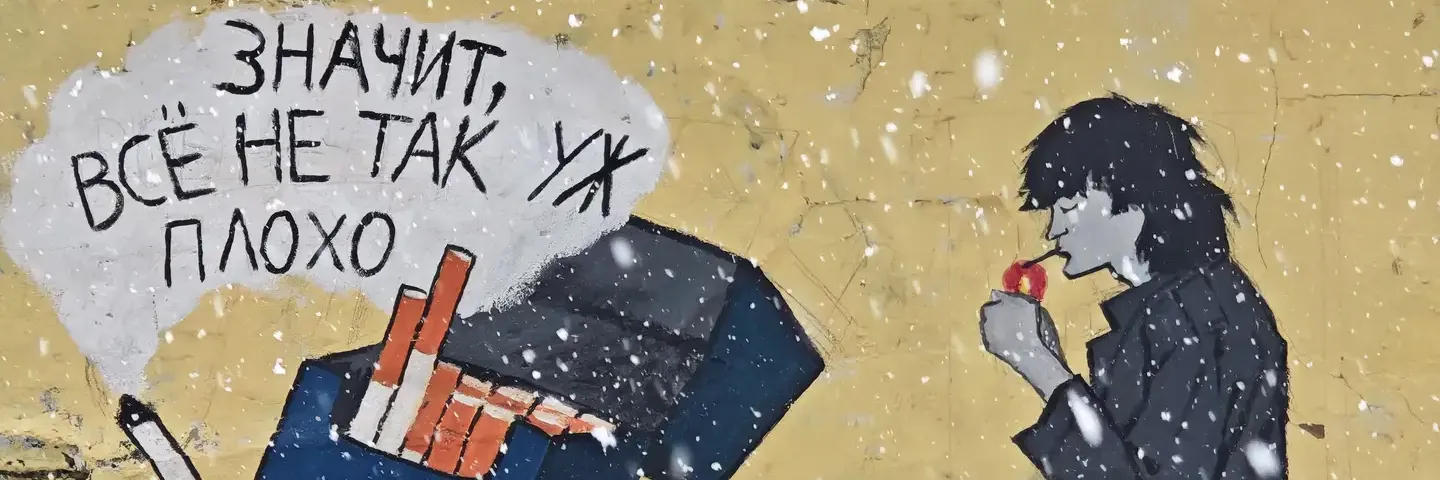 “看来,一切还不至于那么糟” 在一面粗糙的米黄色墙面上,张贴着一幅街头艺术作品,画面左侧是一个倾斜打开的蓝色香烟盒,其中一根香烟伸出盒外。烟盒上方有一团白色的云状烟雾,里面写着黑色的俄文句子“ЗНАЧИТ, ВСЁ НЕ ТАК УЖ ПЛОХО”。画面右侧是一个穿着深色衣服的黑色剪影人物,正点起一支烟,背景中有白色的雪花飘落。
